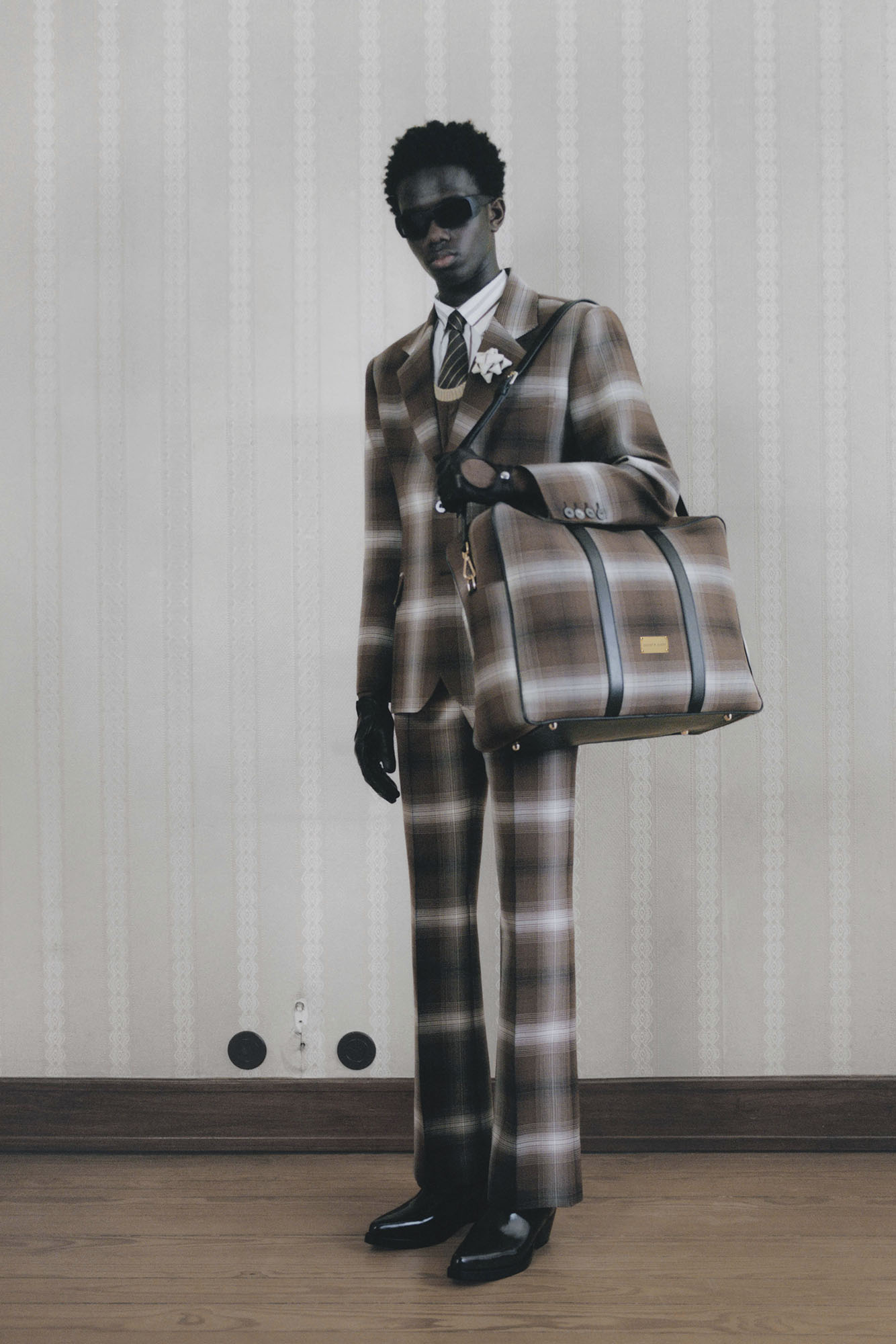 Man in plaid suit with bag in front of white wall