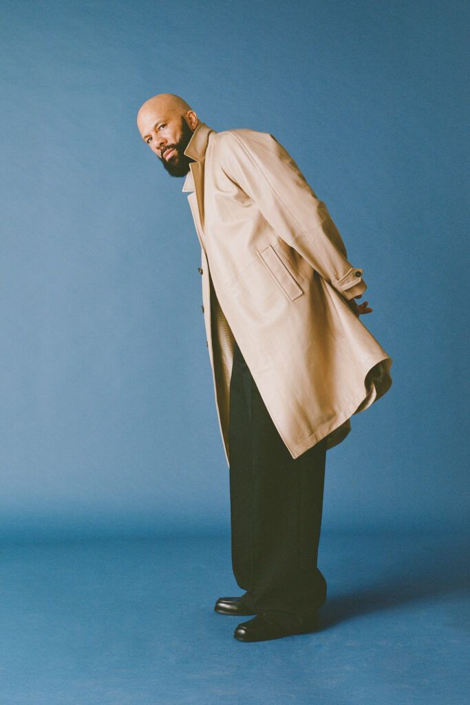 Common wears tan jacket in front of blue background.
