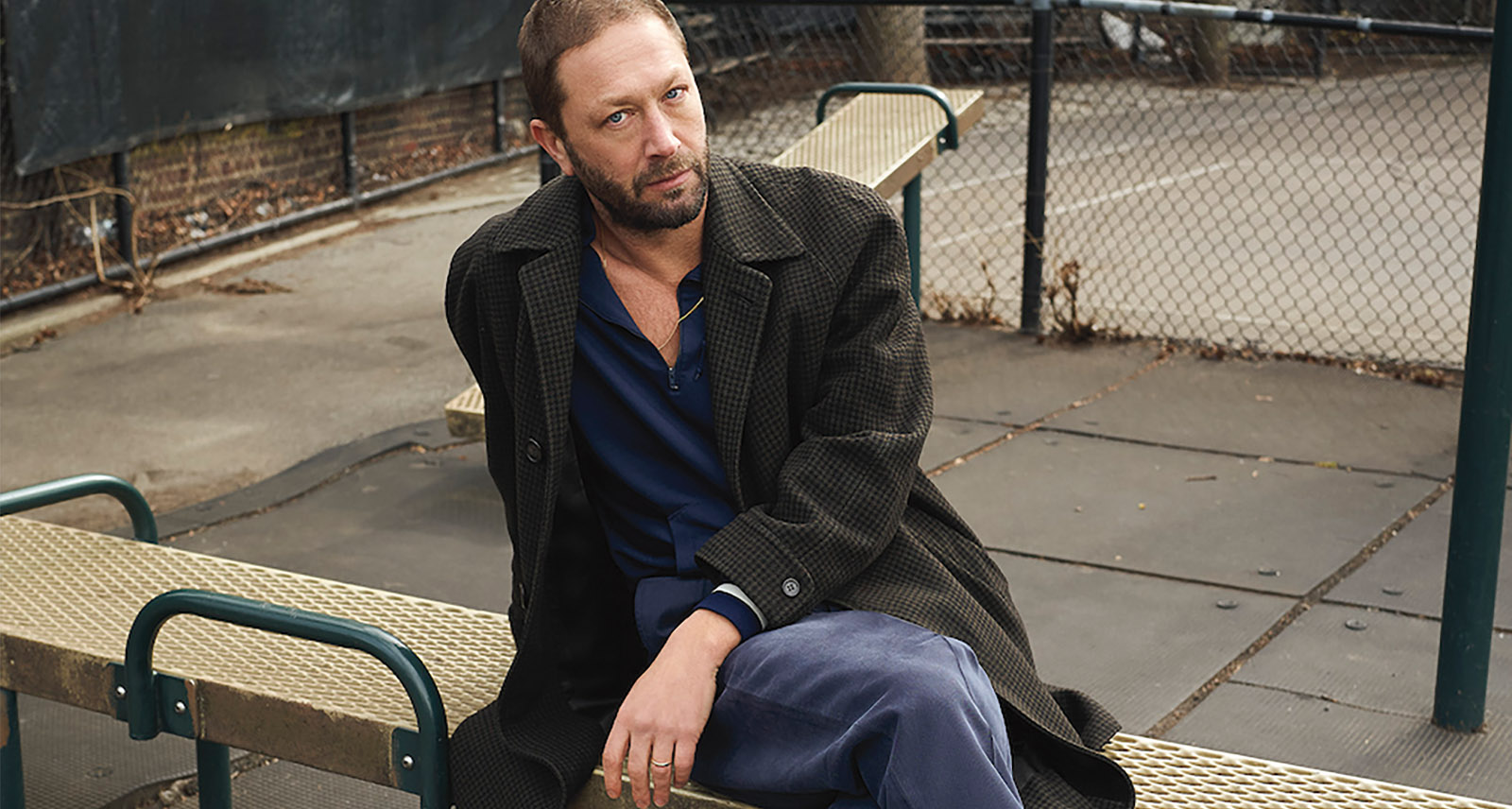 Ebon Moss-Bachrach sits on bench with legs crossed