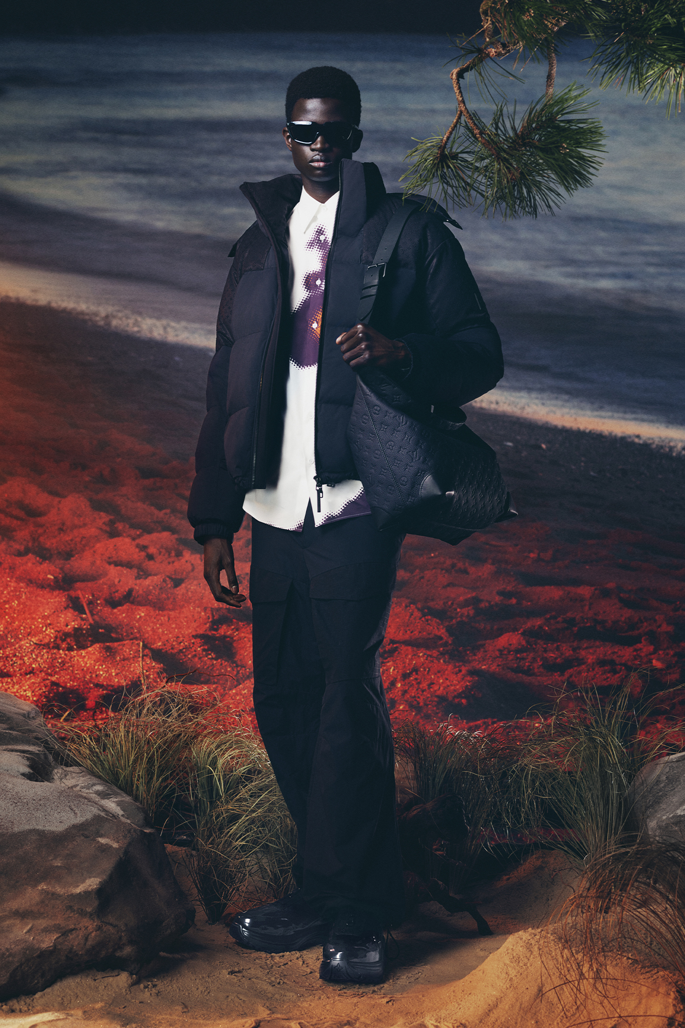 Men's Collection Pre Spring/Summer 2024 model in dark navy jacket, white shirt, and black pants in front of forest and lake backdrop