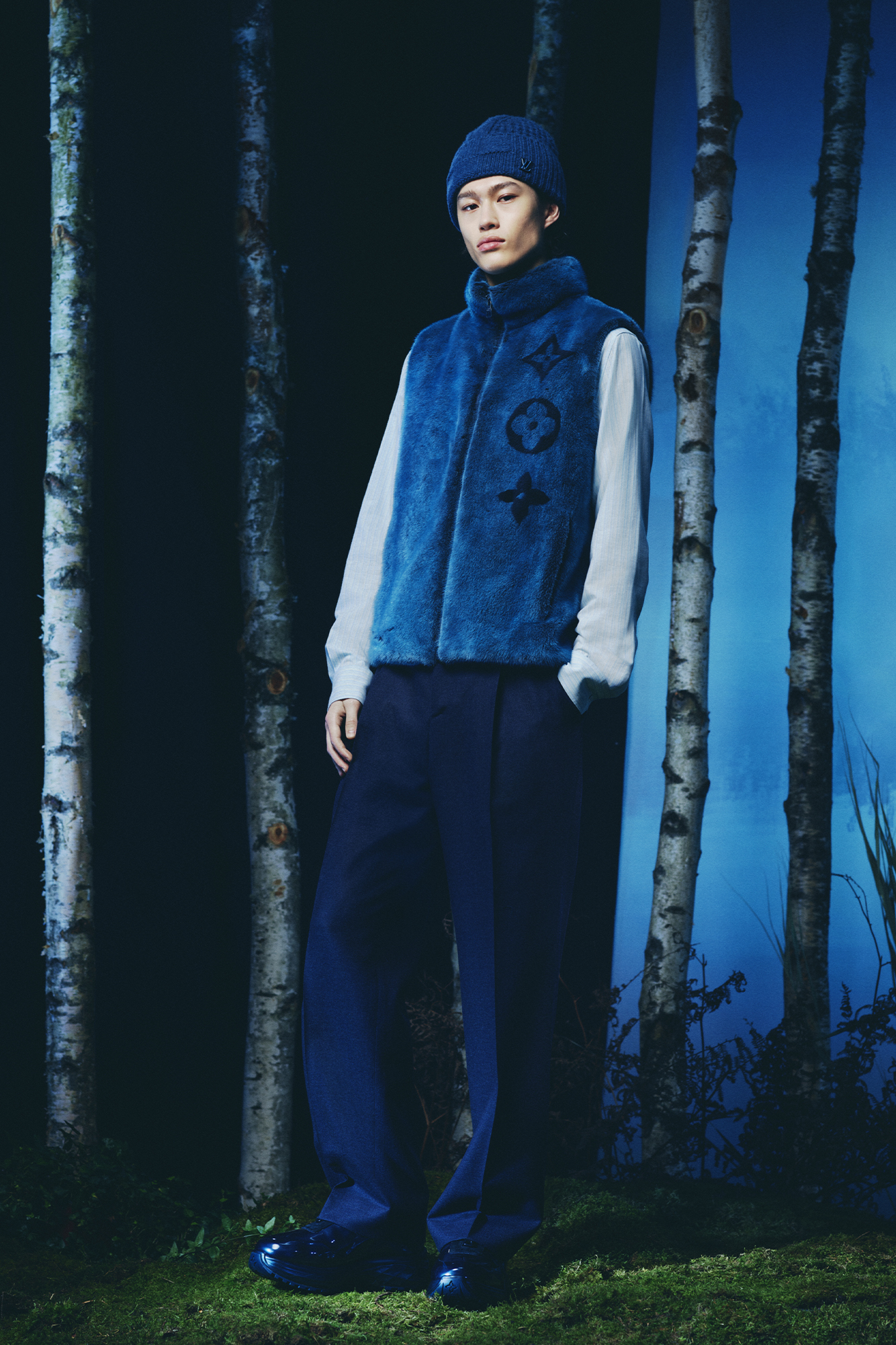 Louis Vuitton Men's Collection Pre Spring/Summer 2024 model in forest wearing blue vest, long sleeve shirt and dark pants