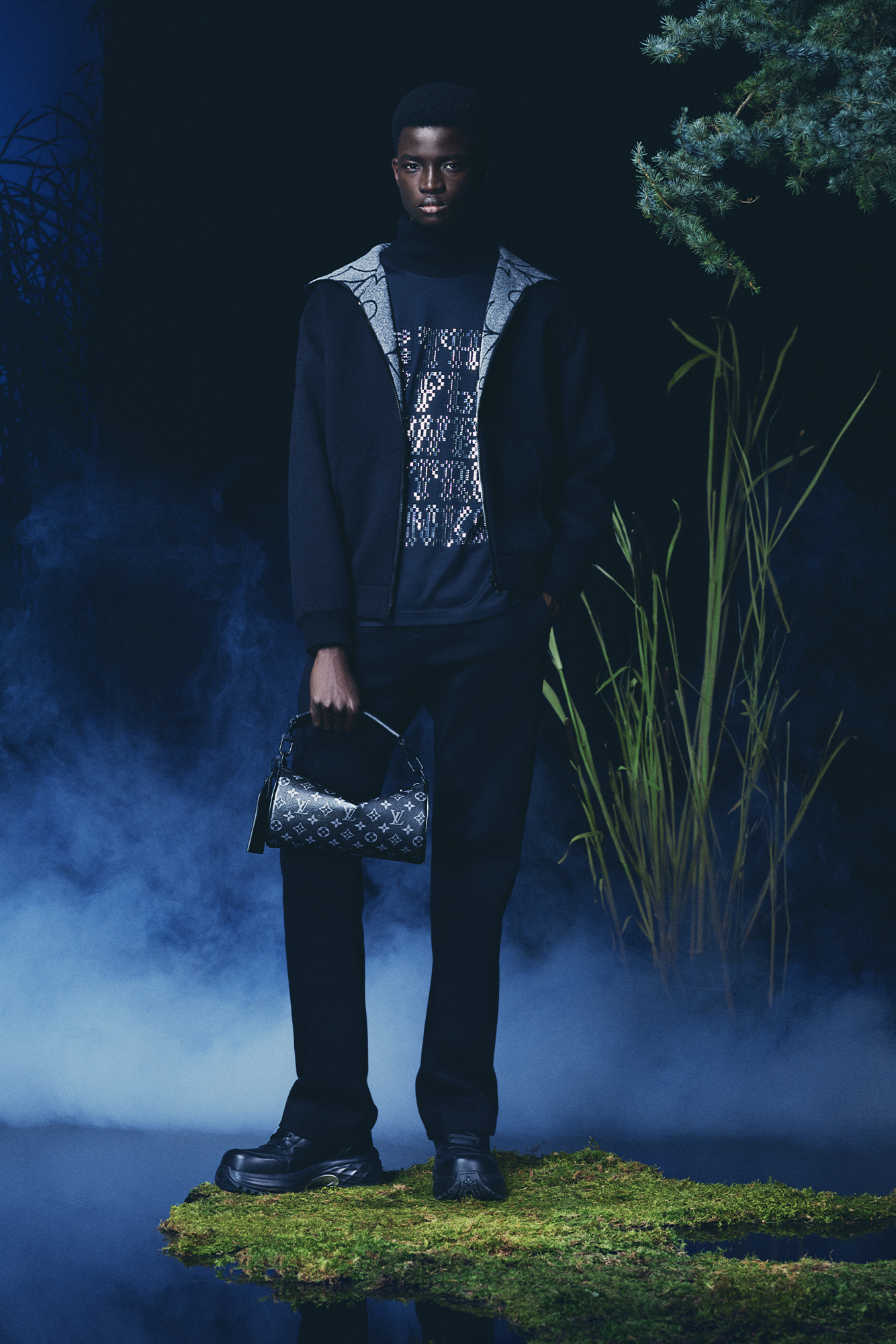 Louis Vuitton Men's Collection Pre Spring/Summer 2024 model in forest wearing dark ensemble with blue highlights
