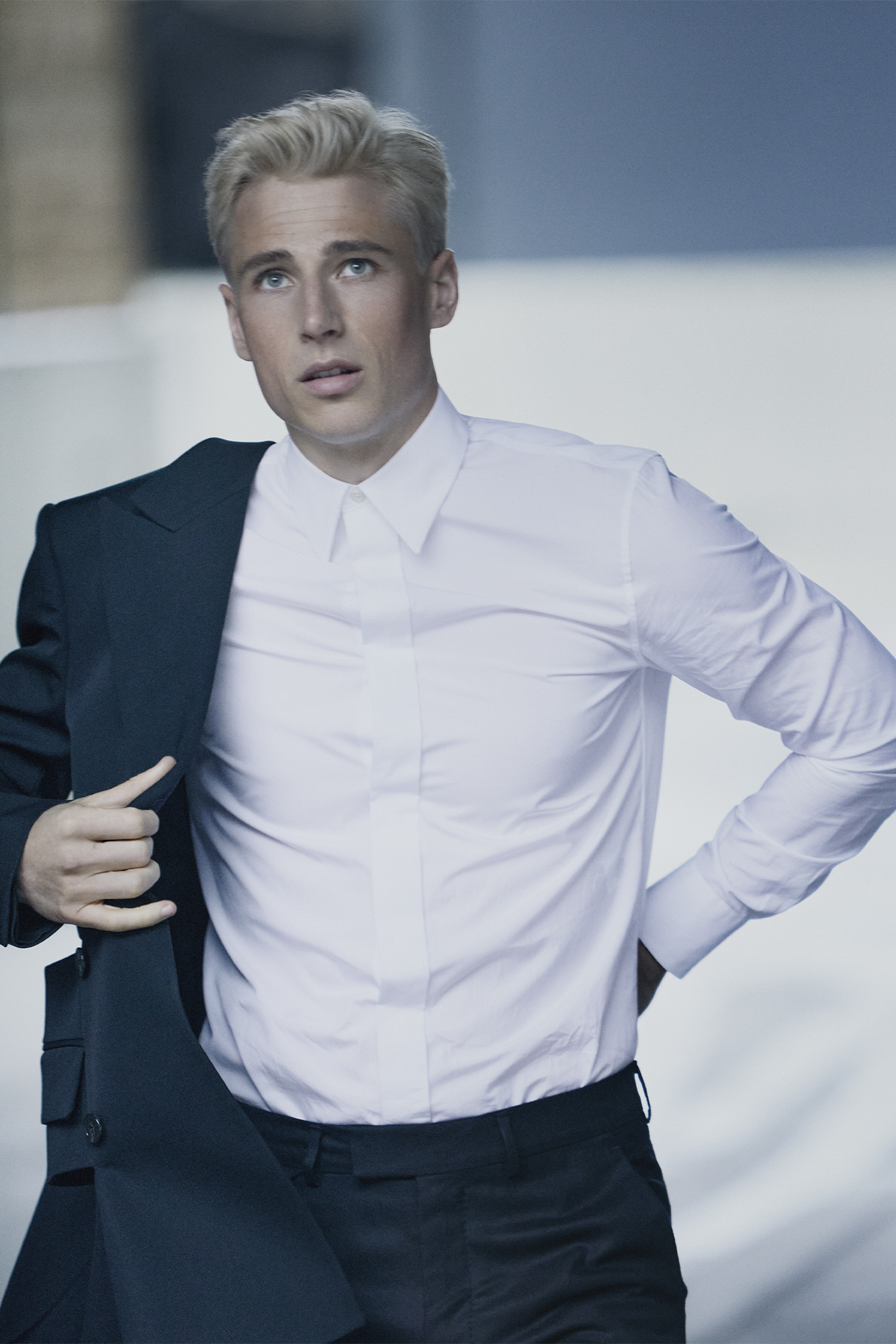 Male model in white shirt putting on a blue jacket and looking up