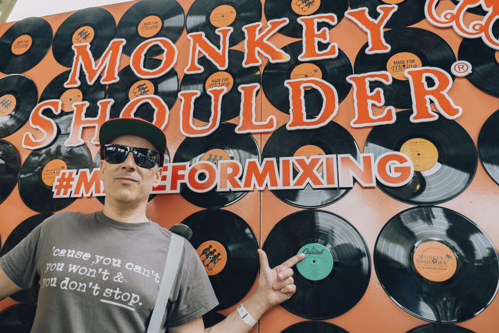 DJ Skratch Monkey Shoulder party man in front of ad board