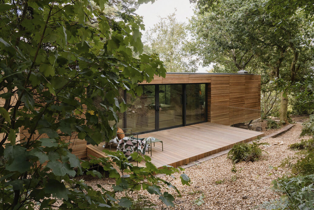 Looking Glass Lodge Uk Home for Rent front side of house framed by trees, wood patio and glass doors