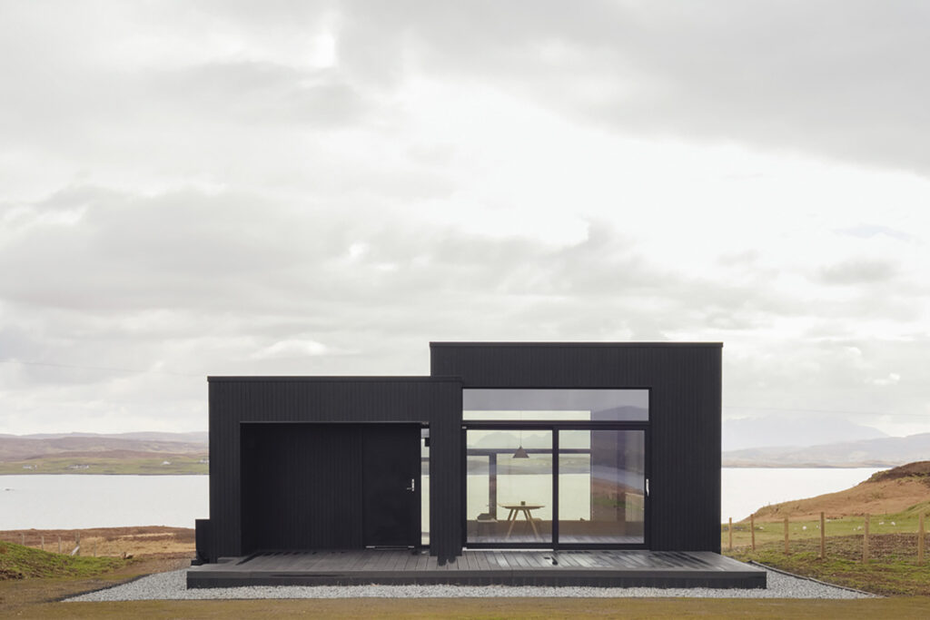 Harlosh Black H Home for rent in UK Scotland black and boxy exterior sits on low-lying green plain. 