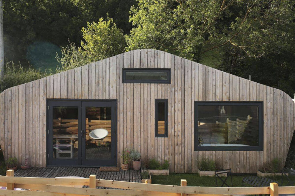 Hergest Lee Cabin & Lean-To Cabin in Wales, UK for rent. exterior is triangle shaped and wooden, with trees in back
