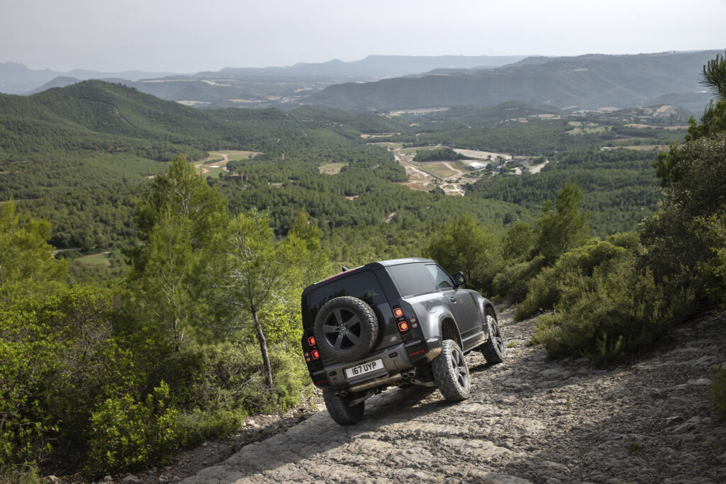 Land Defender 90 boxy suv from the back with tire driving on mountainside 