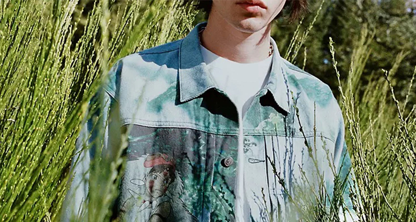 Levis X Princess Mononoke model standing in tall grass shot from lips to waist in denim jacket with white tee