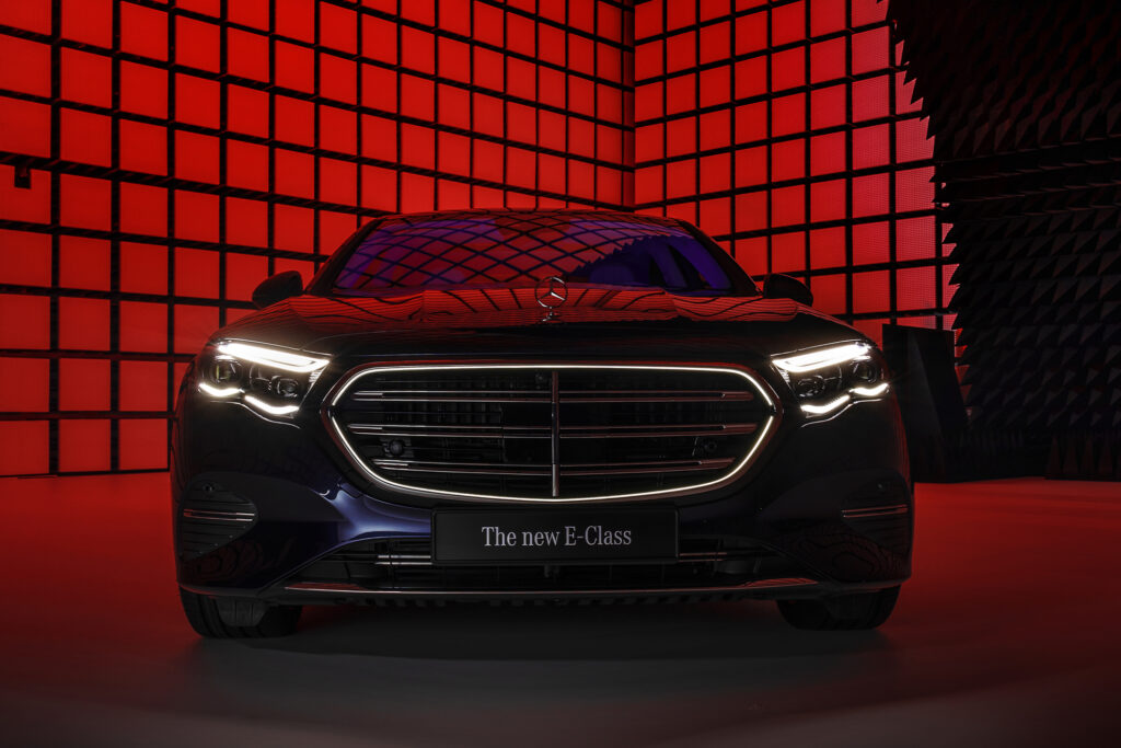A mercedes e-class sedan is parked on a black floor in front of a red-lit grid background