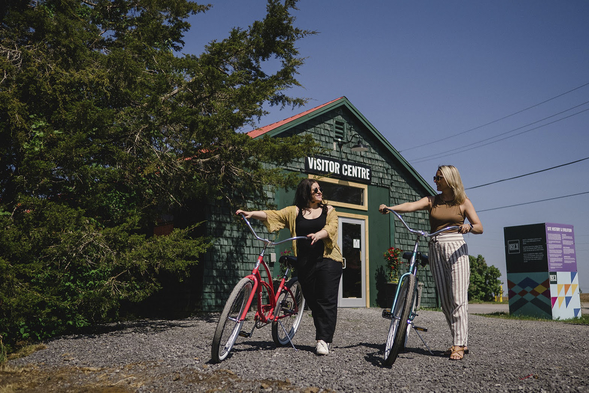 Prince Edward County Taste Trail women wheeling bikes in front of green shingled-building