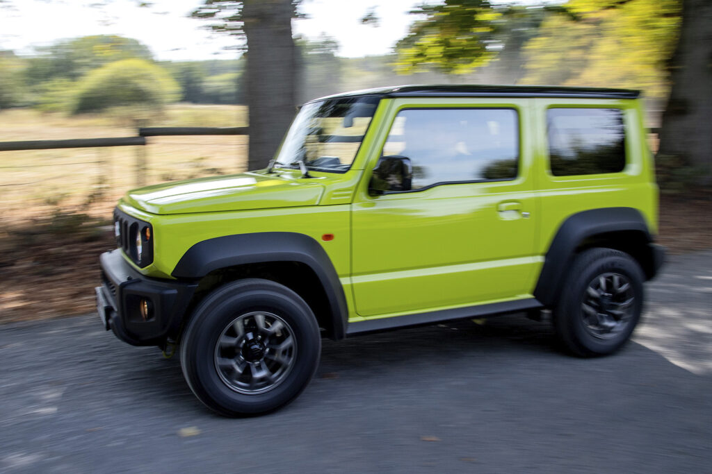 Yellow-lime-green Suzuki Jimny shot from the side, driving on a street during a sunny day