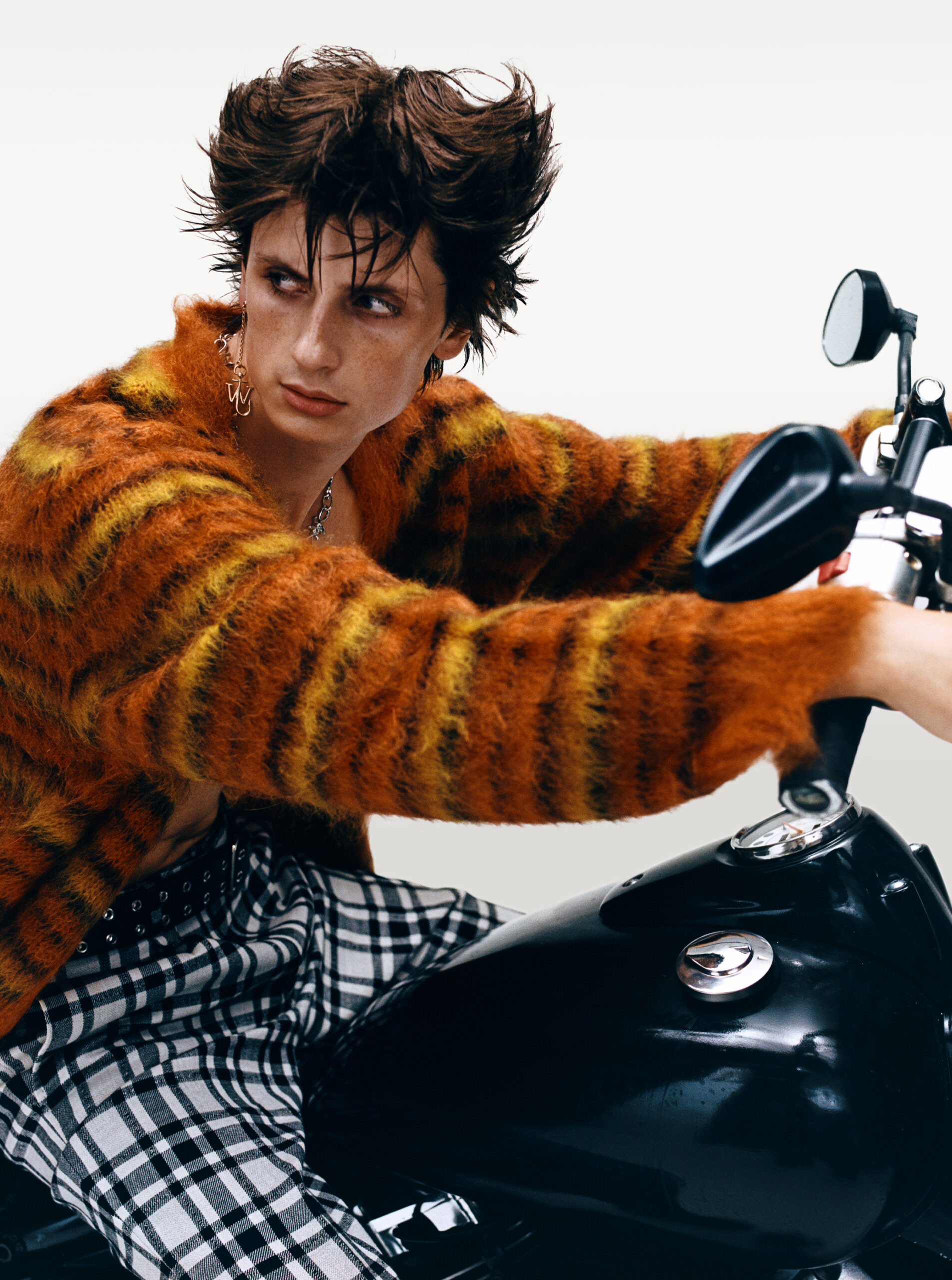 Model riding a motorbike in a fuzzy orange sweater. SWEATER ($1,700) BY MARNI, AND EARRINGS ($375) BY JW ANDERSON, AT SIMONS; PANTS ($495) BY HAROLD, AT HARRY ROSEN.