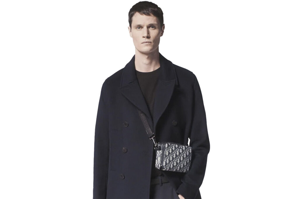 Model wearing Dior double breasted peacoat over dark undershirt with bag