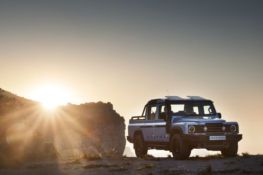 Ineos Grenadier Quartermaster parked next to a rock on a mountain top at sunset