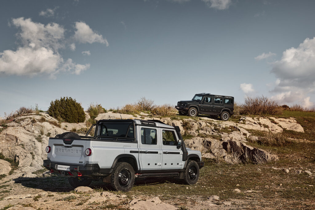 two Ineos Grenadier Quartermasters are parked on a rock clearing; one is silver and one is black