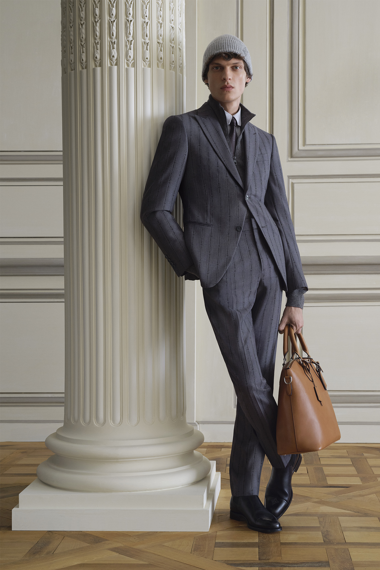 Model at Louis Vuitton spring summer 2024 show leans on pillar in grey suit with bag