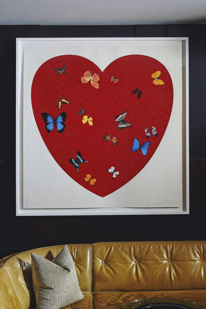 Damien Hirst print of a heart with butterflies hangs above an orange-brown l-shaped leather couch