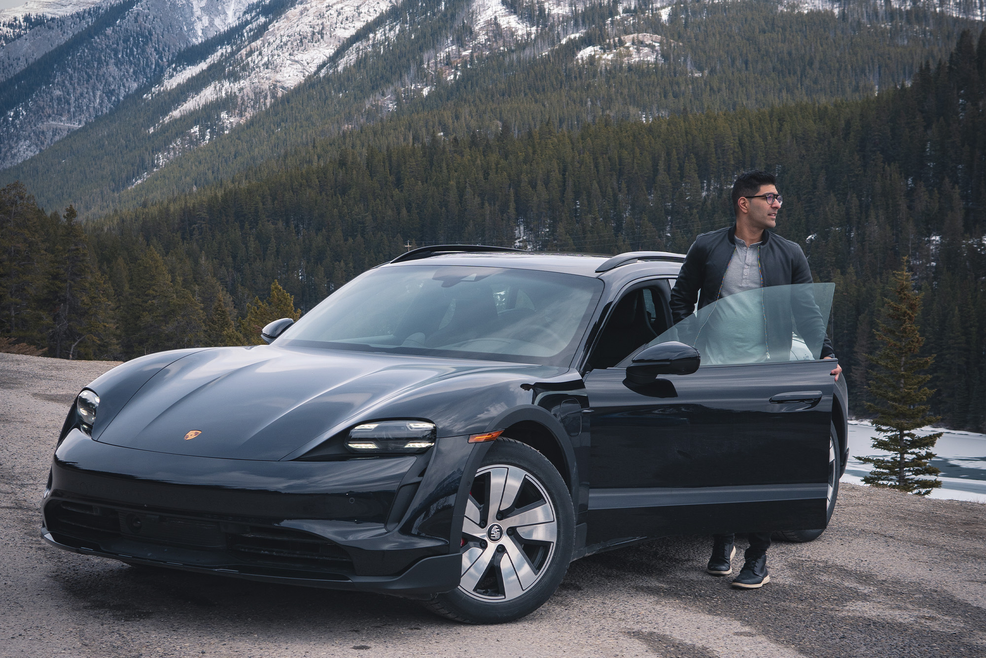 Black Porsche at Panorama Mountain Resort & Greywolf Golf Club. Man in leather jacket steps out of car while it is parked on the street. It's shot from the front at an angle, with mountains in the back