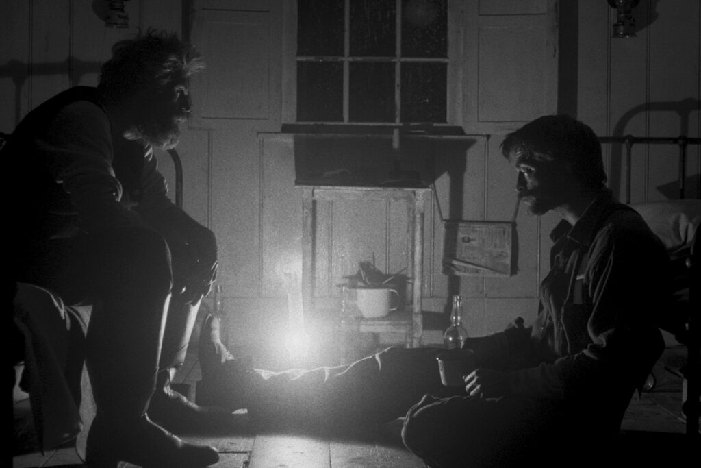 Robert Pattinson and Willem Dafoe chat by candle in black and white photo on Lighthouse designed by set decorator 