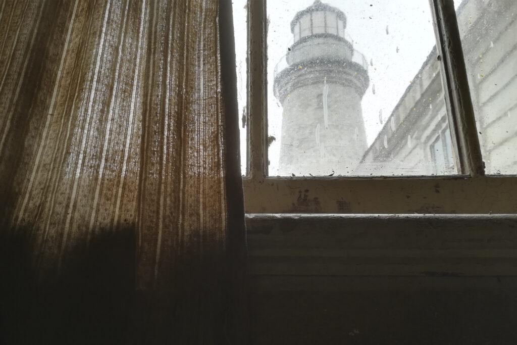 Drying out the curtains by a window that looks out onto a lighthouse