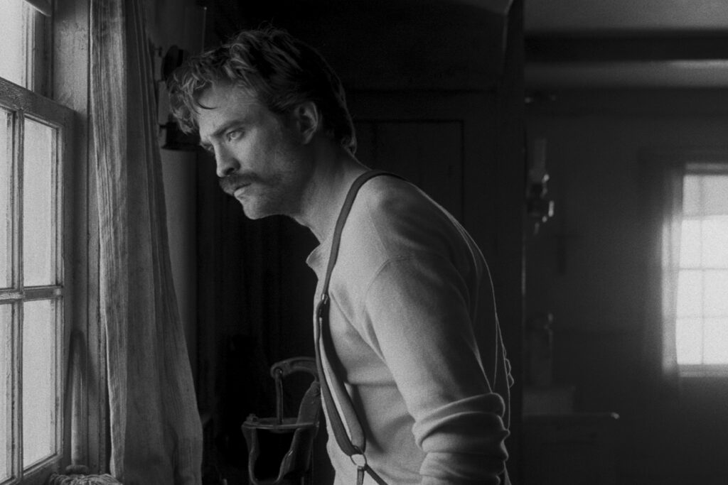Robert Pattinson looks out the window in black and white photo on Lighthouse designed by set decorator 