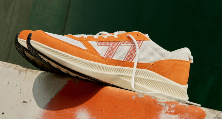 Le TIGRE orange shoe stands on concrete wall, shot from the side