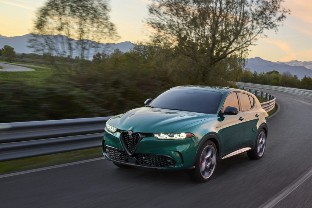 green Alfa Romeo Tonale drives on a road at sunset with mountains and trees in the background