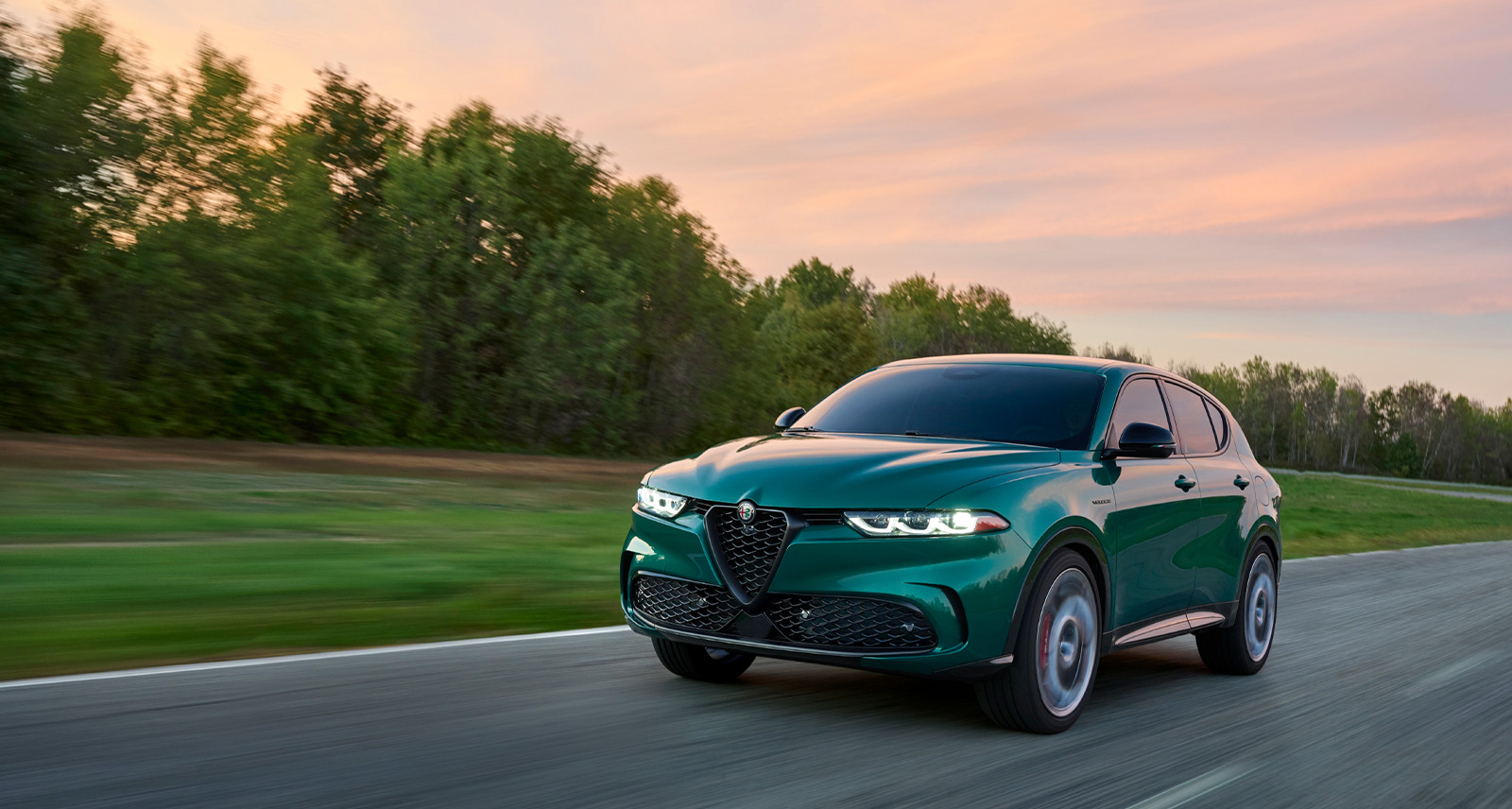 Green Alfa Romeo Tonale drives along a highway at sunset there are trees in the back