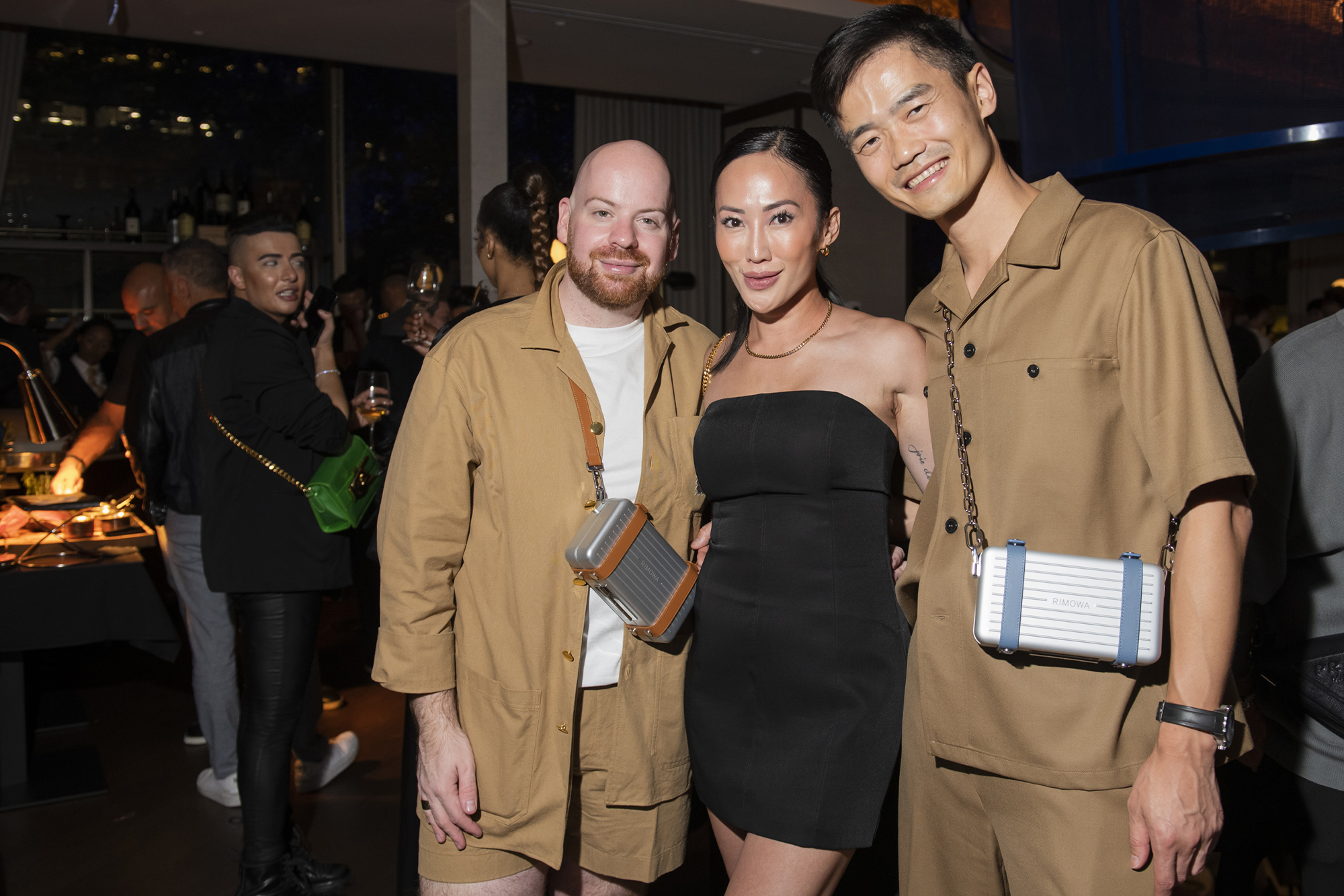 Three guests pose for Bad Boy Cobalt launch party at Black+Blue Toronto. Two men in beige outfits are on the right and left of a woman in a black dress.