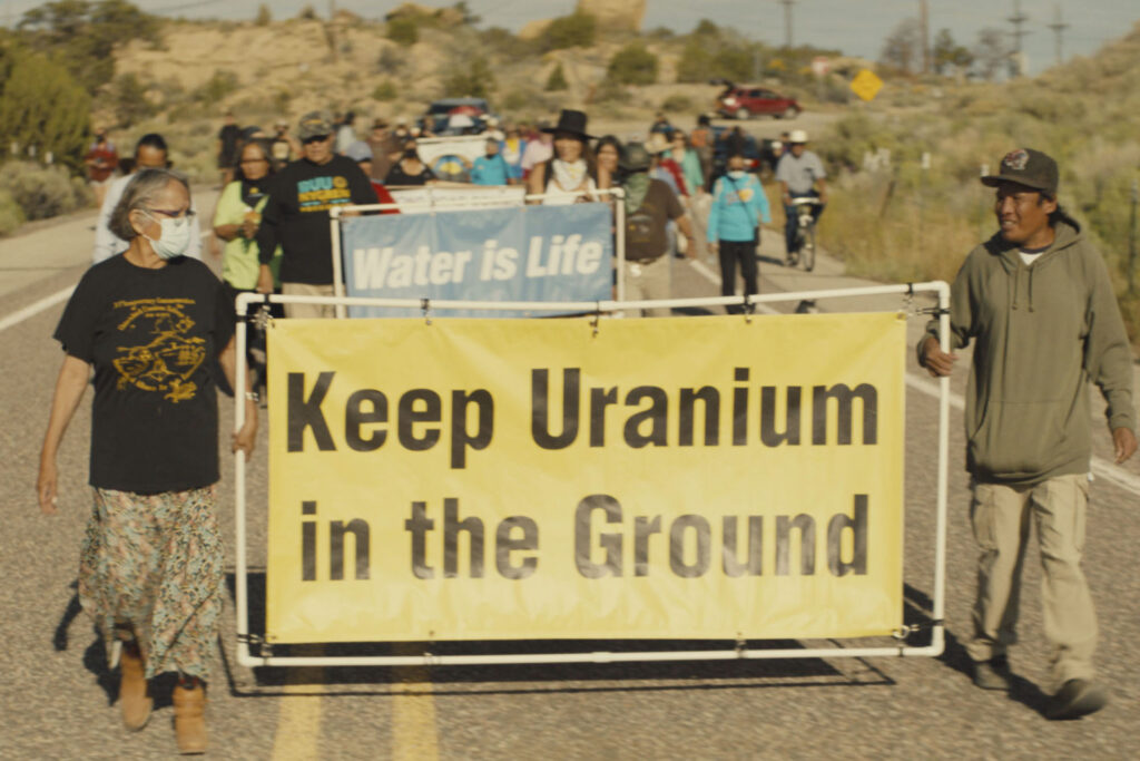 Film still shows people marching with a sign that reads 'keep uranium in the ground,' in Boil Alert