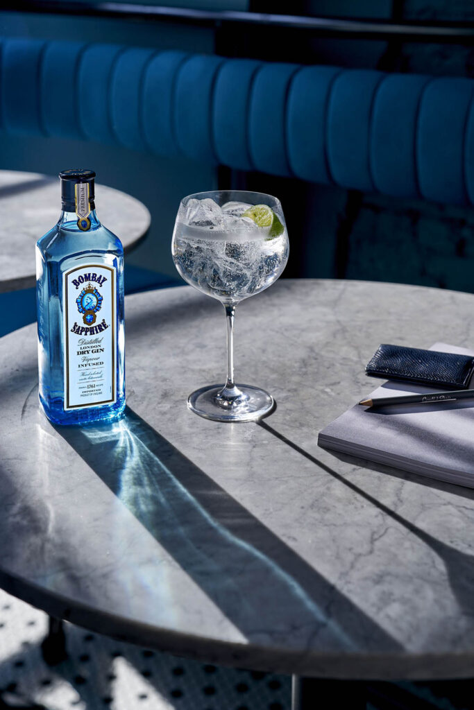 Blue bottle of bombay gin on a table next to a glass 