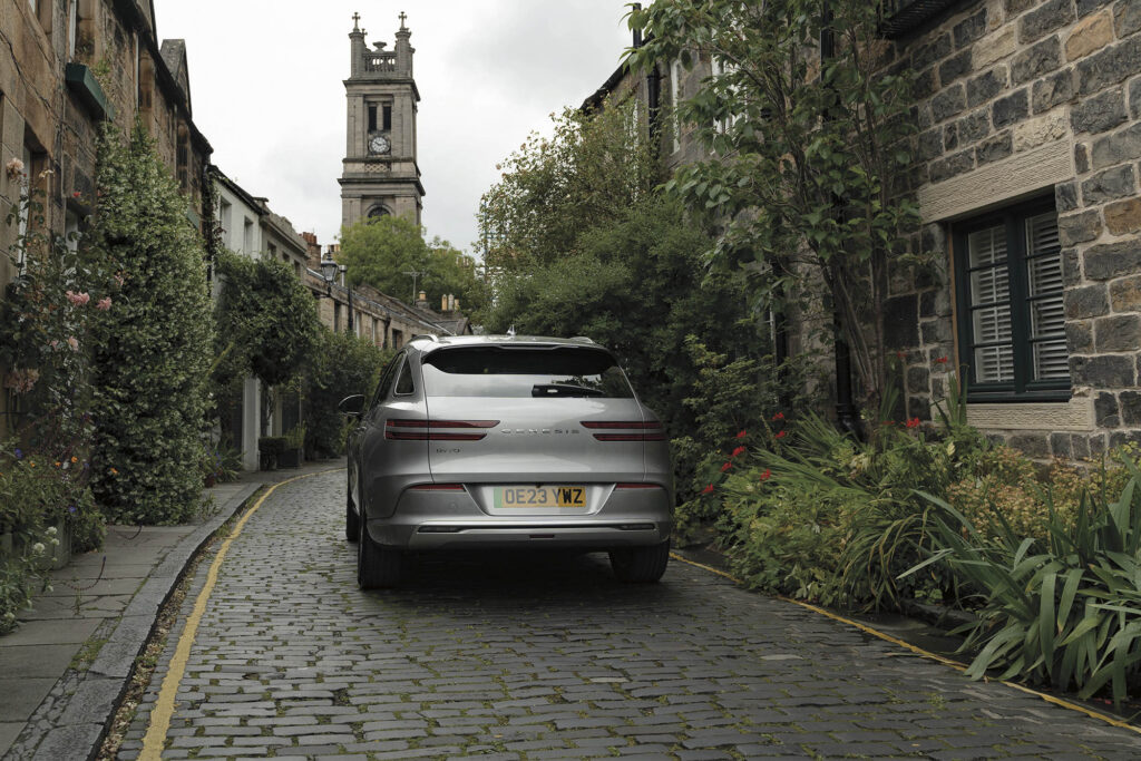Genesis Electrified GV70 rear view as it drives up cobblestone street