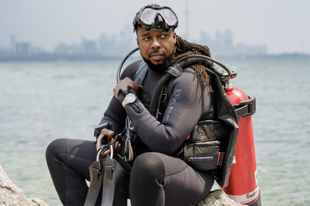 JNiice poses by the ocean in full scuba gear before a dive