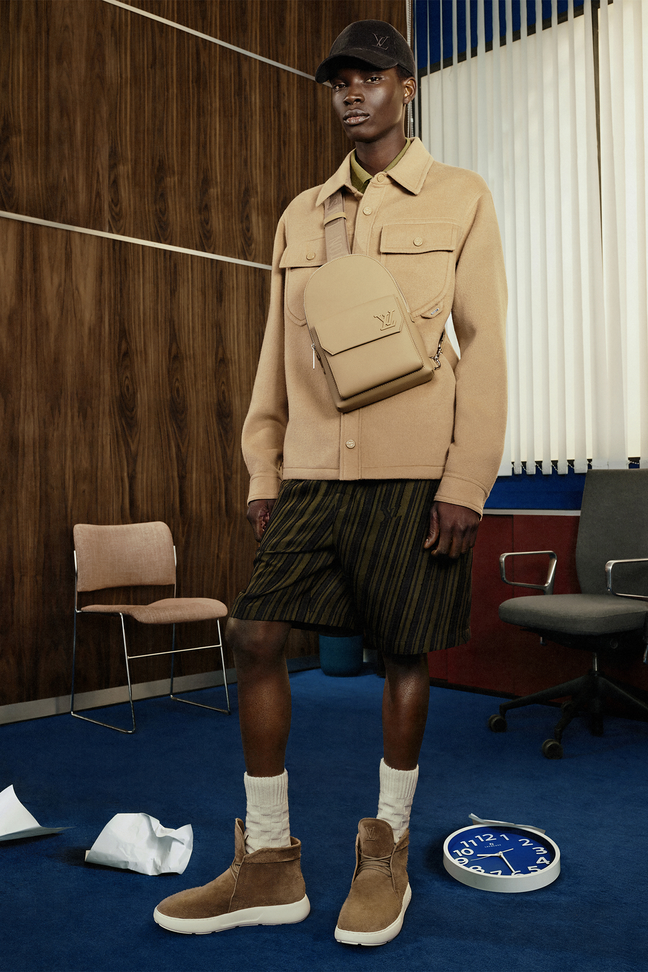 Model in beige jacket and bag with black shorts and cap, and brown shoes for Louis Vuitton Studio Prêt-à-Porter Homme