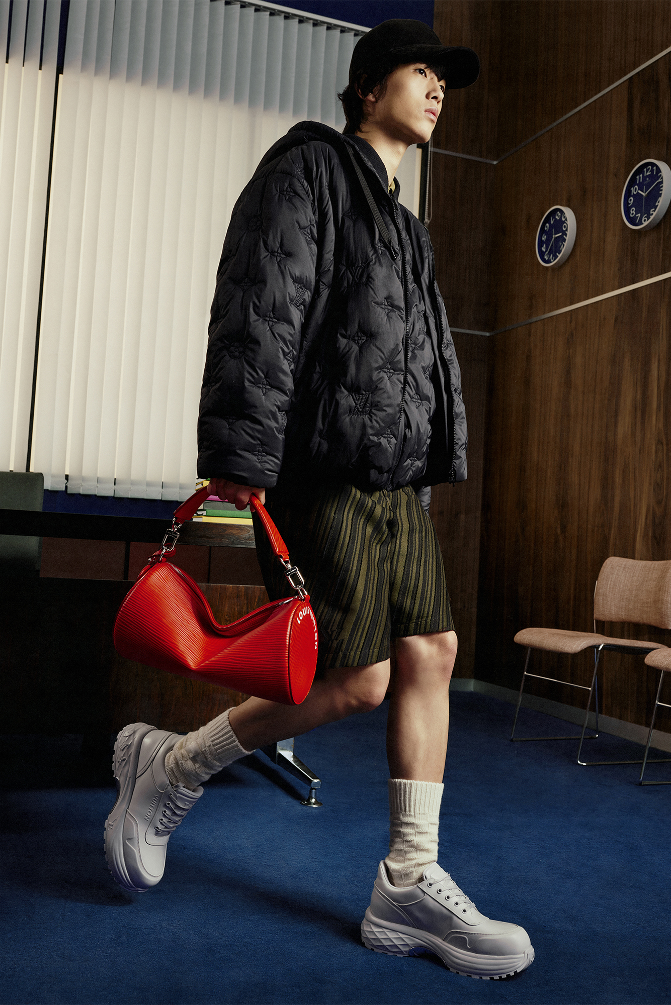 Model with black jacket and dark green shorts carrying a red bag for Louis Vuitton Studio Prêt-à-Porter Homme