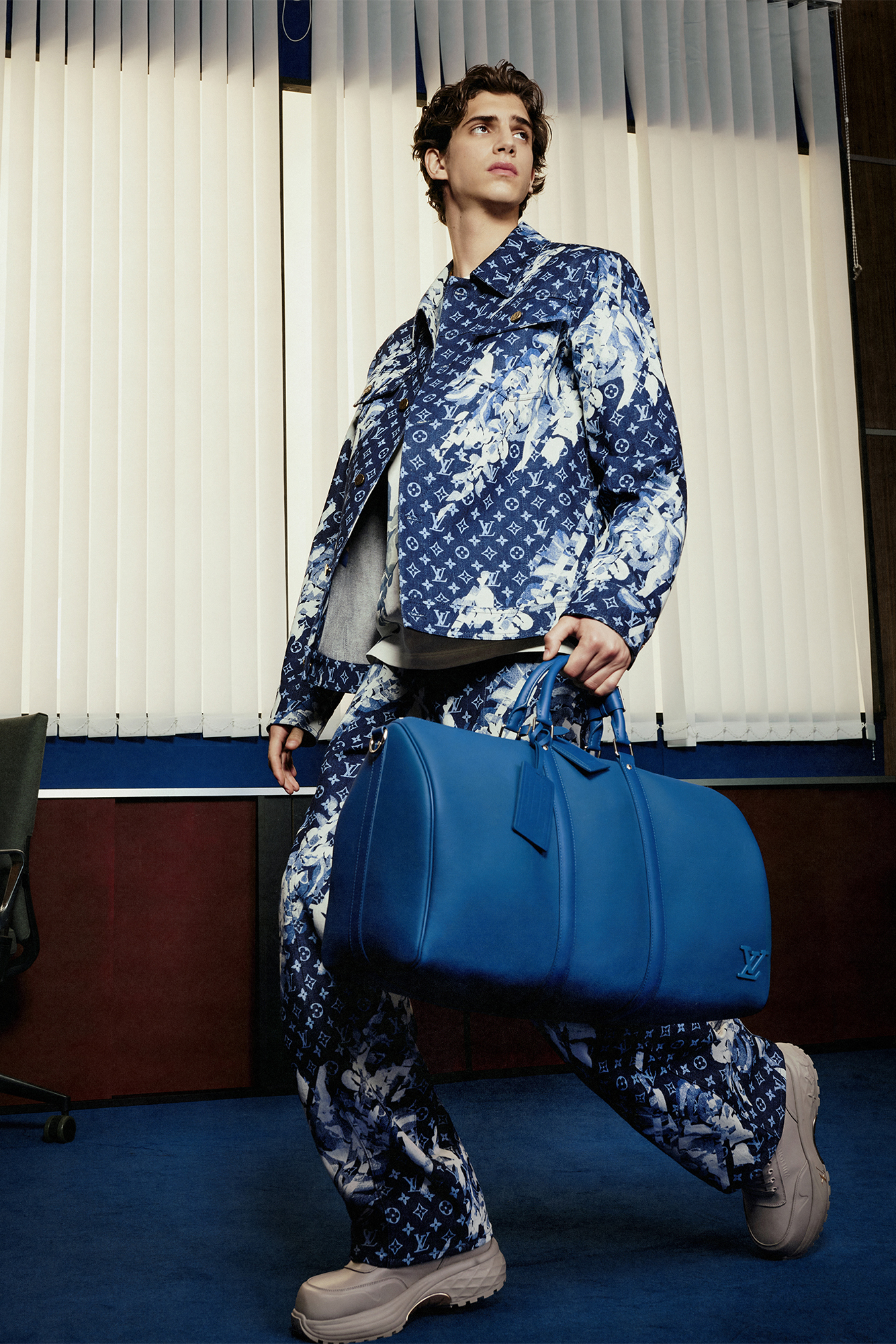 Model in denim/acid wash Louis Vuitton monogram jacket and pants with blue bag