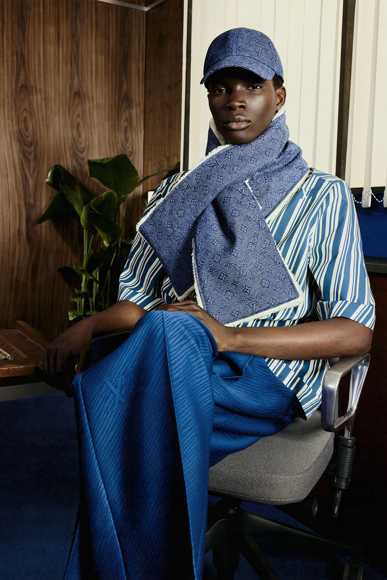 model in scarf and hat sitting down on a chair with legs crossed for Louis Vuitton Studio Prêt-à-Porter Homme