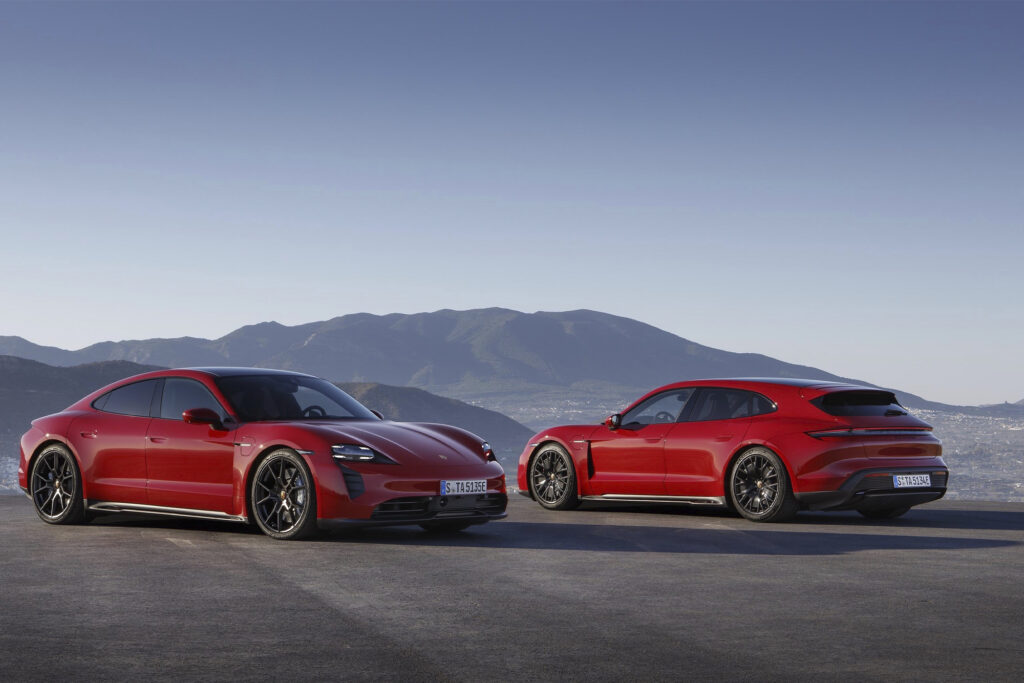 two red Porsche Taycan GTS parked in opposing directions by a mountain on a road