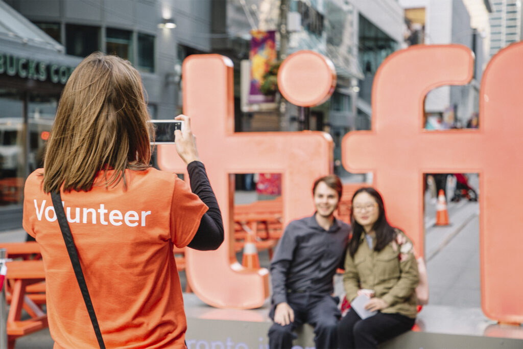 Volunteer takes photo of a couple posing by TIFF sign