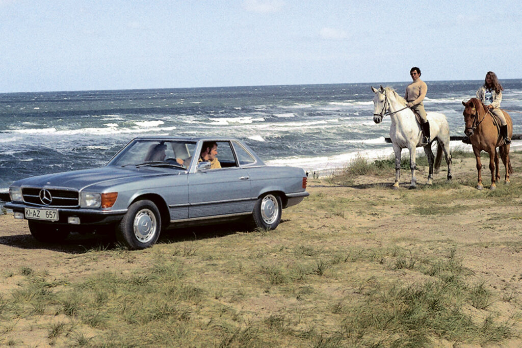 couple on horses on a beach by a blue parked car