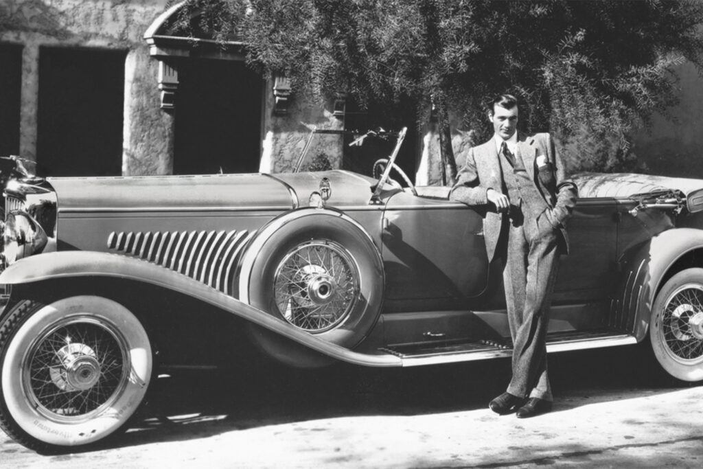 a man in a black and white photo next to an old car
