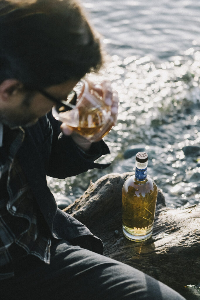 a man drinks bearface whisky on a rock by the ocean