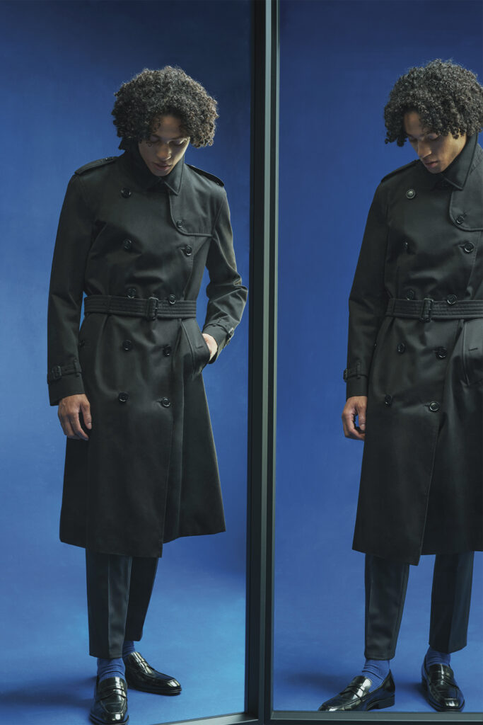 Model wearing a black trenchcoat on a deep blue background
