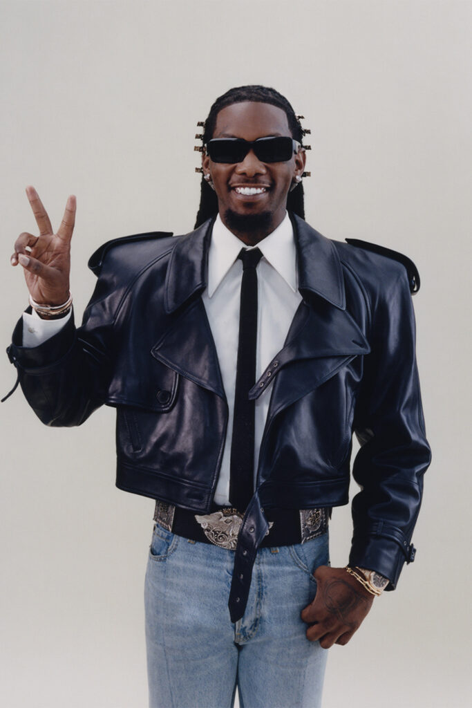 Offset interview on off the wall for Sharp November; rapper gives a peace sign in prada glasses, leather jacket, shirt, tie, and jeans with big belt