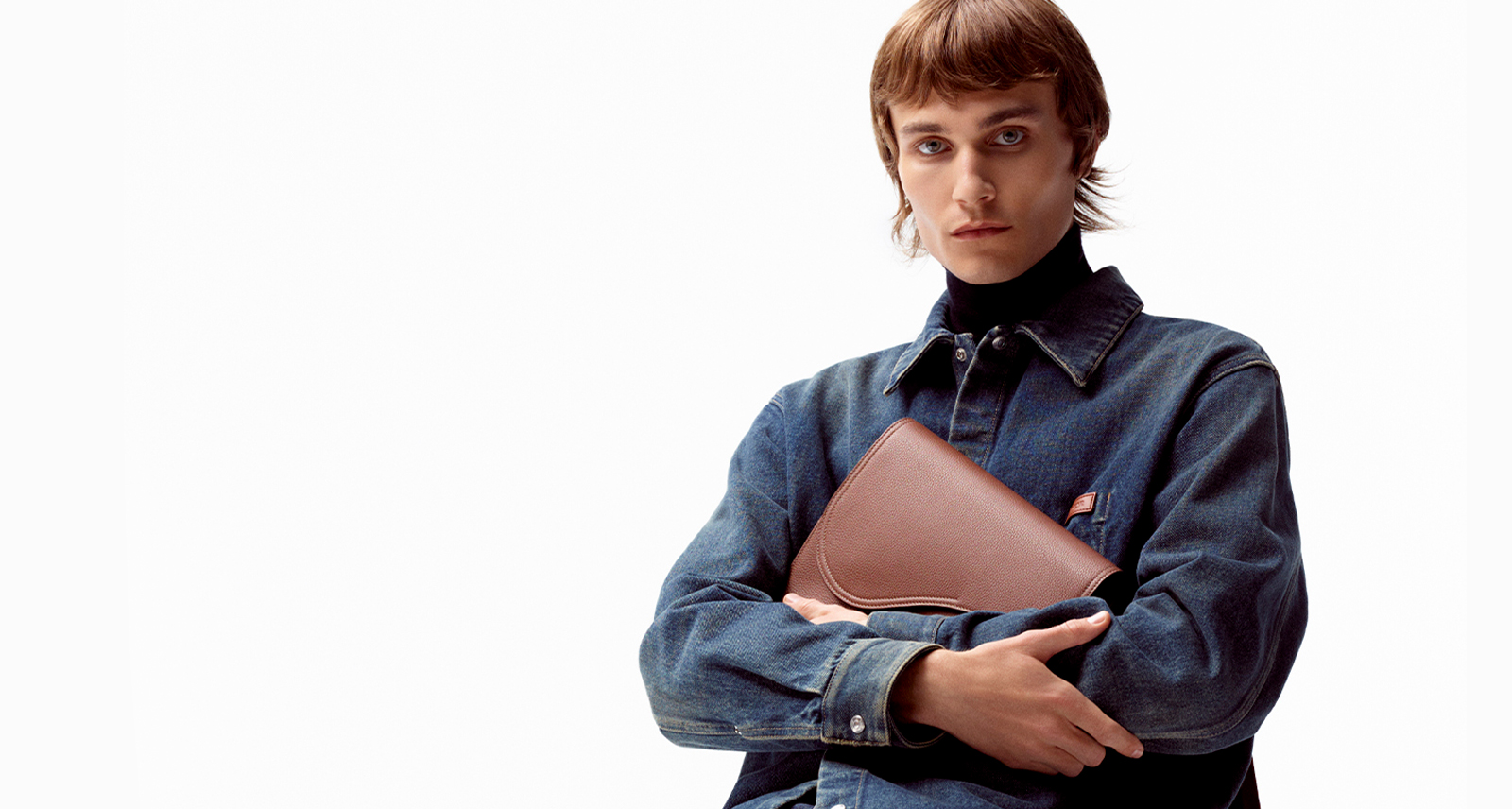 man for dior denim capsule holding a leather case and wearing a denim jacket