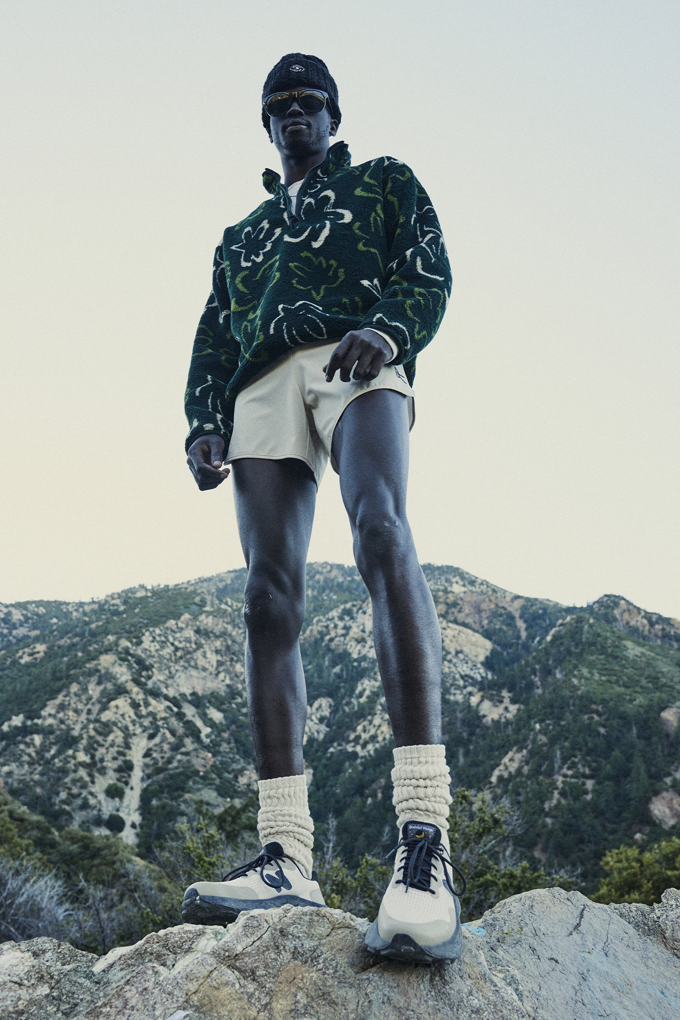 man stands atop a mountain, wearing white shorts and a running jacket