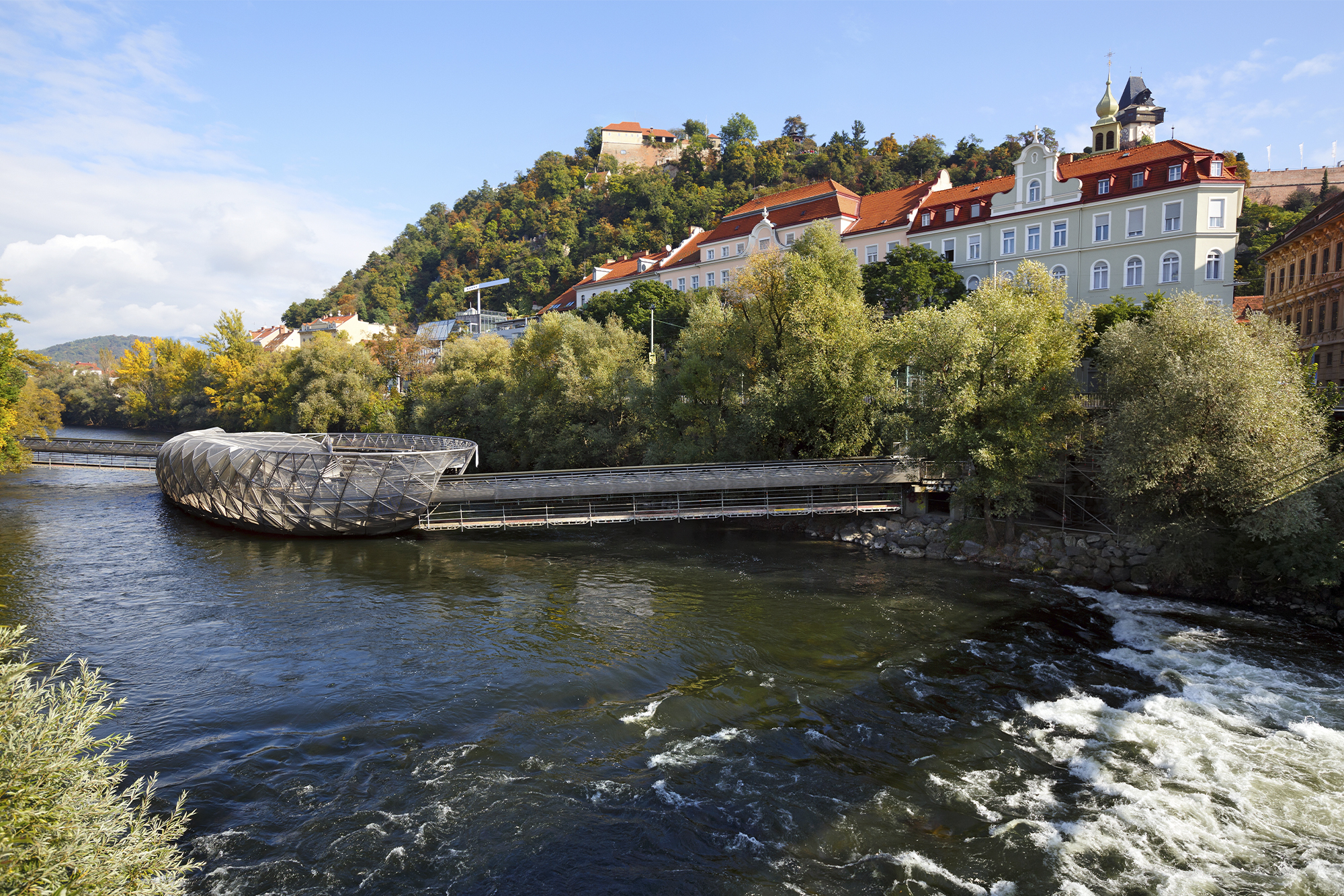 River Mur with the artificial floating platform Mur island (Murinsel) in the middle and old buildings on the river bank Graz Austria