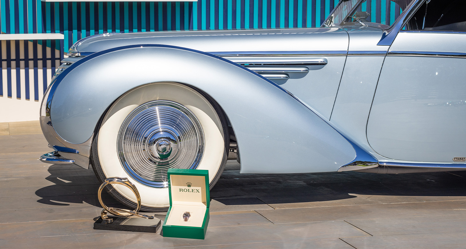 Monterey Car Week Rolex close up of vintage blue car and front wheel with rolex watch placed in foreground 9-2024