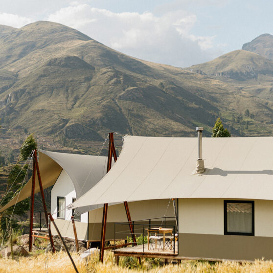 PUQIO Tented Resort in Southern Peru, photo of exterior showing white tented roof on a sunny field with mountains in the background